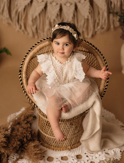 Toddler girl milestone portrait session by Tamara Danielle,  Toronto Newborn Photography session, dressed in white frills on wicker chair boho scene.