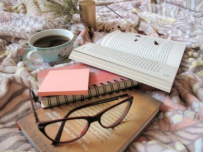 Books, glasses and a cup of coffee resting on top of a blanket.
