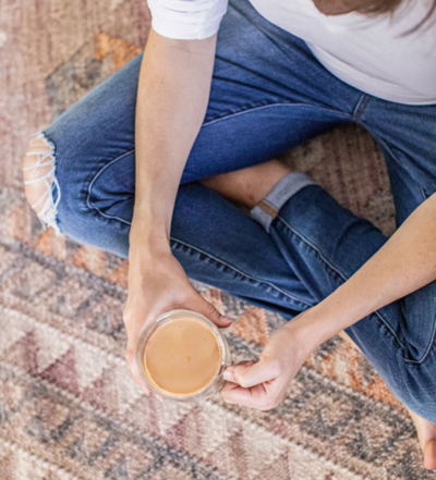 Birds-eye-view of a woman sitting on a rug holding coffee