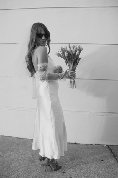A woman in a wedding dress, bouquet in hand, smiles with a videography duo, celebrating the joyful occasion.