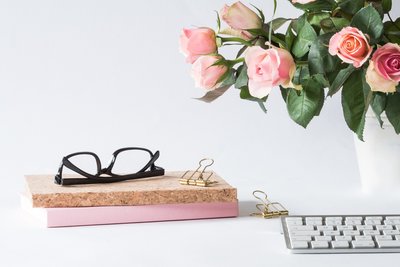 Black glasses on a stack of books next to  vase with pink roses