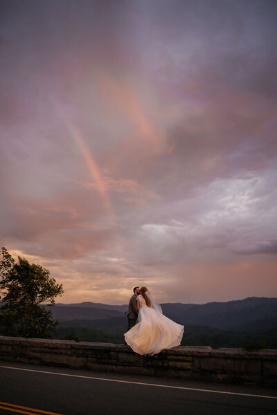 couple eloping to gatlinburg at Harper's Vineyard with the couple holding each other while standing under the brides veil in a field at sunset with the smokies in the distance at the Gatlinburg wedding venue