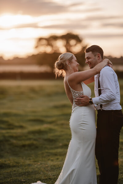 Bride and groom laughing at golden hour in a field during couple portraits