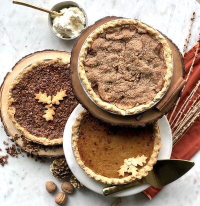 Three pies on platters; Pecan Pie, Pumpkin Pie, and Dutch Apple Pie from left to right.