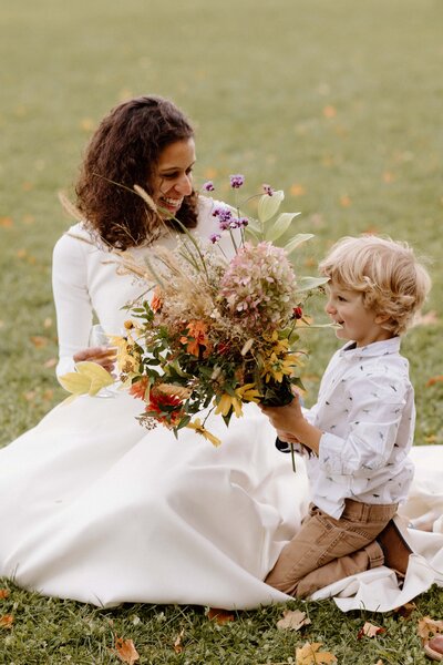 The bride's son giving her mother a bouquet of flowers after the wedding.