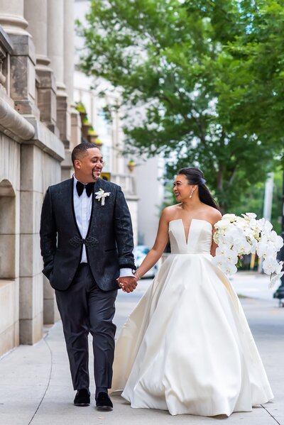 Bride and groom walk down the sidewalk holding hands on their wedding day