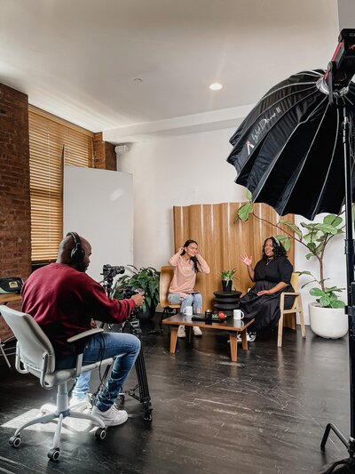 two women being filmed by one man behind camera