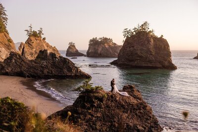 The groom leans over to kiss the bride at a rugged beach during sunset.