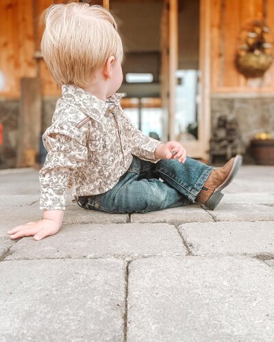 Toddler in jeans, shirt and cowboy boots looking away from camera.
