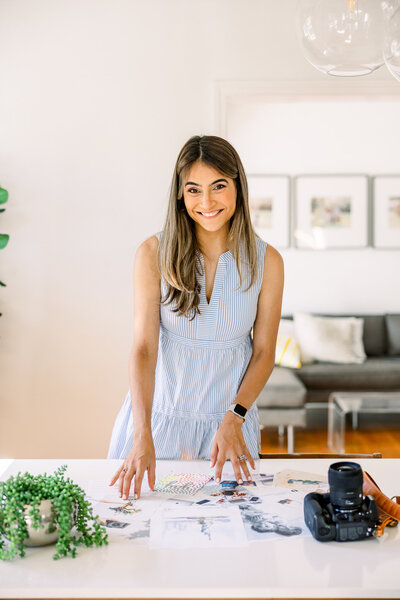 Portrait of Nicole Neira, a Connecticut-based newborn and family photographer, smiling while reviewing prints and photography gear—capturing her warm, creative personality.