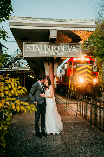 Eloping couple shares a kiss at Staunton VA train station as a red locomotive approaches