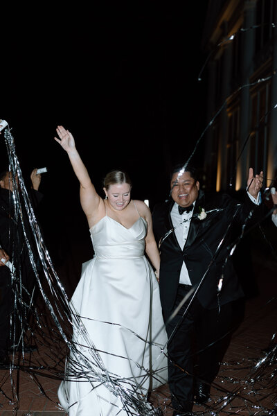 Joyous newlyweds exit their wedding venue under a sparkling tunnel of sparklers held by guests, celebrating their first steps as a married couple.