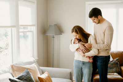 mom kisses newborn's forehead with dad holding hand
