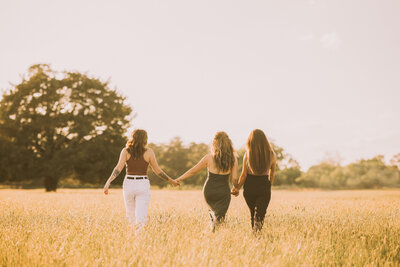 three women holding hands while walking through a field
