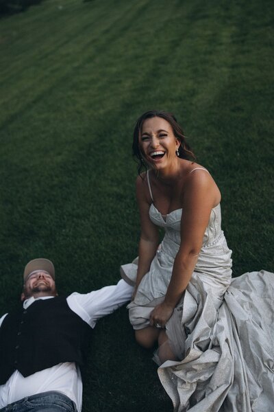 Bride and groom laugh as they roll in the green grass in their backyard.