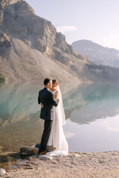 The bride and groom stand together at Bow Lake, embraced by the lake’s vibrant turquoise waters and surrounded by the majestic Rocky Mountains, creating a breathtaking scene of natural beauty.