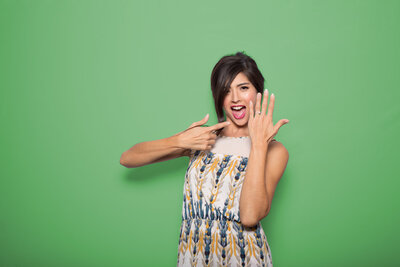 A lady posing for a picture in a photo booth pointing her other hand with green background