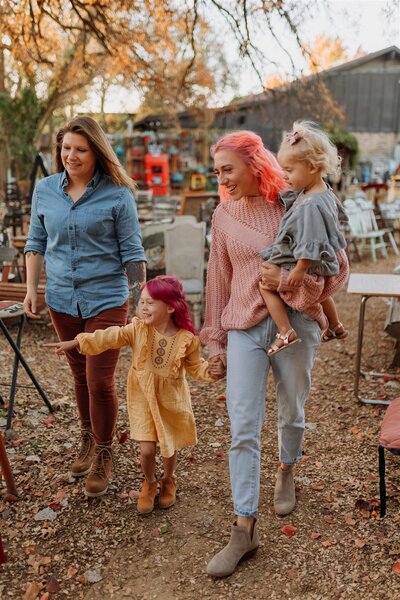 moms walk through area with bunch of chairs while holding onto their daughters