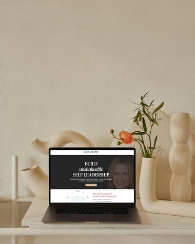 Laptop displaying 'Build Unshakable Self-Leadership' website on clean desk with small plant and neutral background.