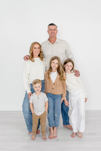A family of five dressed in neutrals smiling at the camera in a white studio
