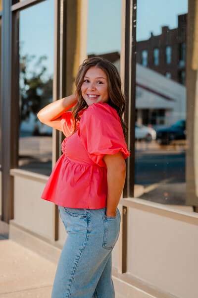 Teenage girl wearing jeans and a bright pink top poses in front of building.