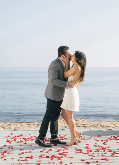 Groom proposing to his fiancee at the beach surrounded by red roses