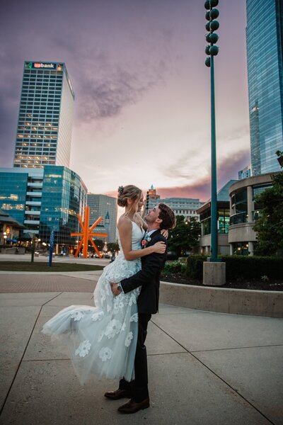 bride and groom outside the milwaukee skyline groom holds the bride up and twirls her