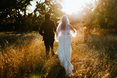 bride and groom walking through field backlit by sun