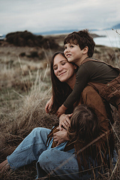 A woman stands in a grassy field at sunset, holding the hand of a small child who looks up at her — a perfect moment captured by Illawarra motherhood photography.