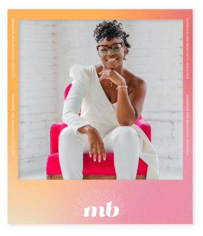 black female chicago photographer smiling in white suit and hot pink chair