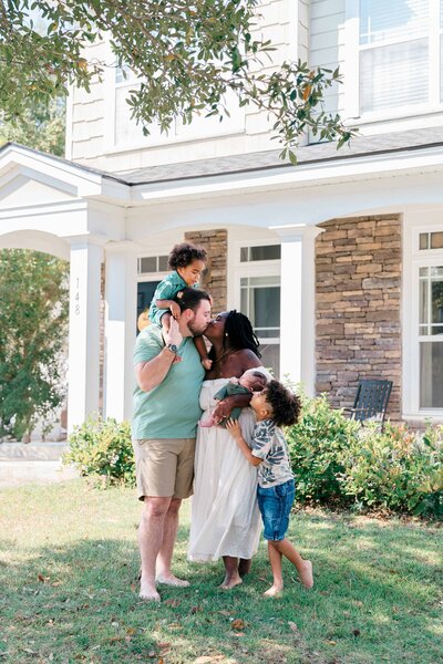 Mom and Dad kiss while holding their children during their in-home newborn session for Bluffton newborn photographer Lamp and Light Photography.