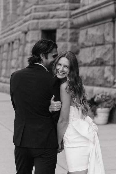 Woman clutches to man's arm and smiles back at the camera as they walk on St. Paul city sidewalk.