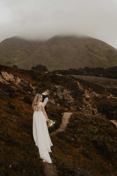 bride walking through hills  with groom