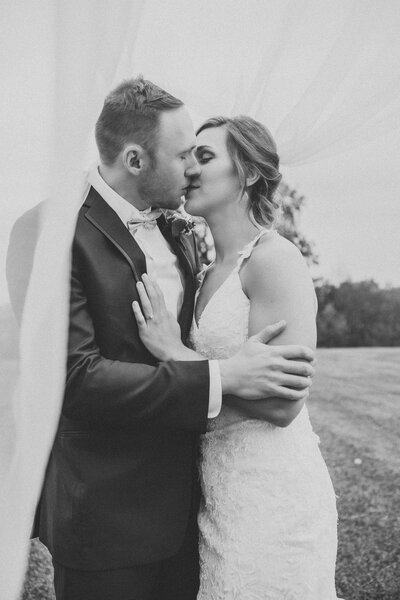 Black and white photo of groom and bride kissing with veil blowing around them  by Iowa City wedding photographer Sabrina Wilham