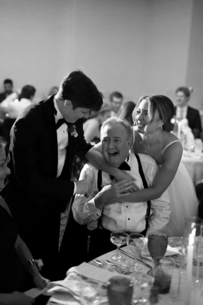 Groom and bride hugging a family member in black and white during a reception