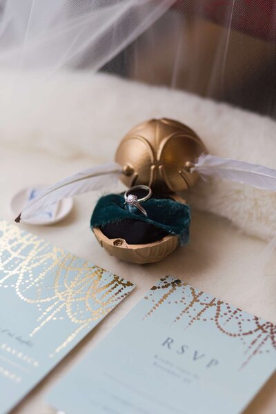 engagement ring sits in a golden snitch above a wedding invitation at Hotel Zaza in Houston Texas by Swish and Click Photography