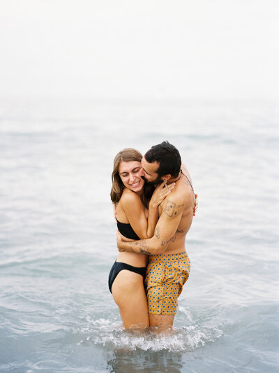 Couple laughs while kissing in the water during their adventurous photo session in Mexico for their vacation.