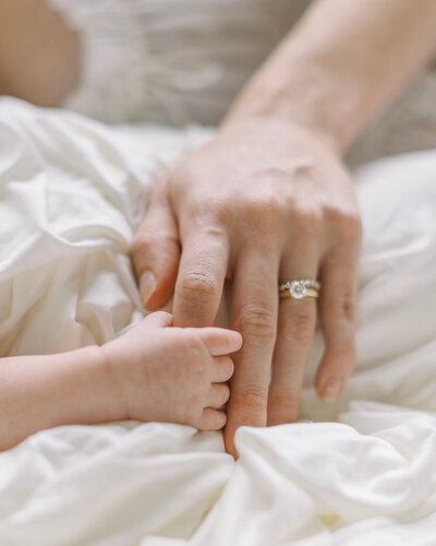  Richmond Newborn Photographer | Closeup photo of a mother’s hand holding her newborn son’s fingers on a white blanket 