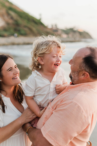 A family laughs and smiles on the beach while taking family photos in Los Angeles.