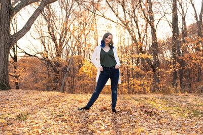 High school girl stands among the fall leaves.