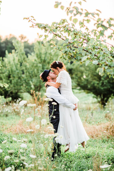 bride and groom kissing in apple orchard at sunset in vermont wedding