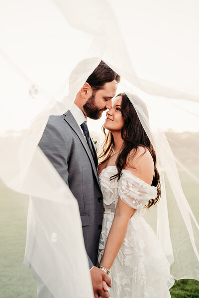 Romantic Willowbend Country Club wedding in Cape Cod, MA, featuring a dreamy golden-hour portrait of the bride and groom wrapped in her flowing veil. Captured by Moll, this intimate moment showcases love, elegance, and the breathtaking beauty of this luxury golf course venue. Perfect inspiration for couples planning a timeless New England wedding!