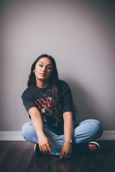 A photographer for seniors Britt Elizabeth captured an image of a woman sitting on the floor, dressed in jeans and a t-shirt.