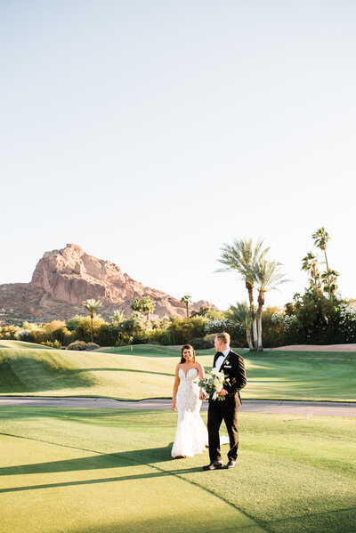 bride and groom walking on the golf course with arizona mountains in background