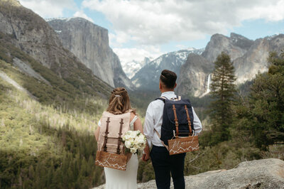 Married couple looking at a mountain view during their Hiking wedding with backpacks that say "Just married"