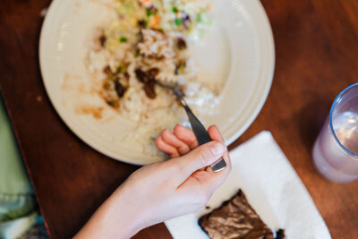 person holding fork and eating rice and beans from white plate