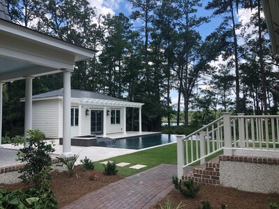 Backyard with pool, pool house, pergola, and landscaping surrounded by trees.