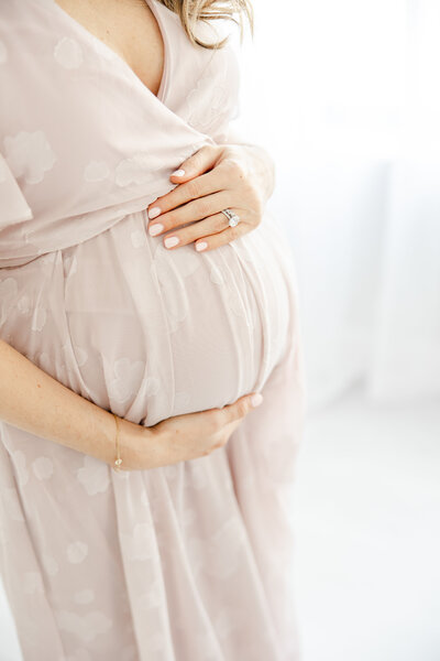 Pregnant woman embraces her belly in blush flowing dress