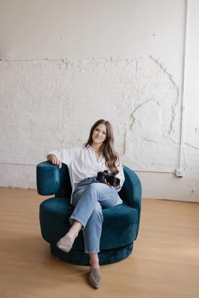 Omaha Wedding Photographer Anna Brace smiles at the camera while wearing blue jeans and a grey top