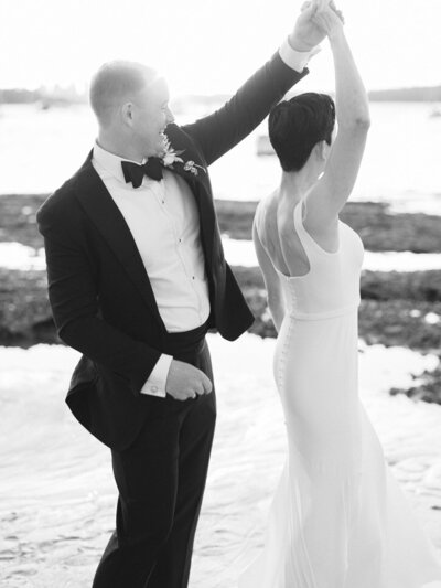 Bride and groom sitting on rocks at beach looking at wedding rings